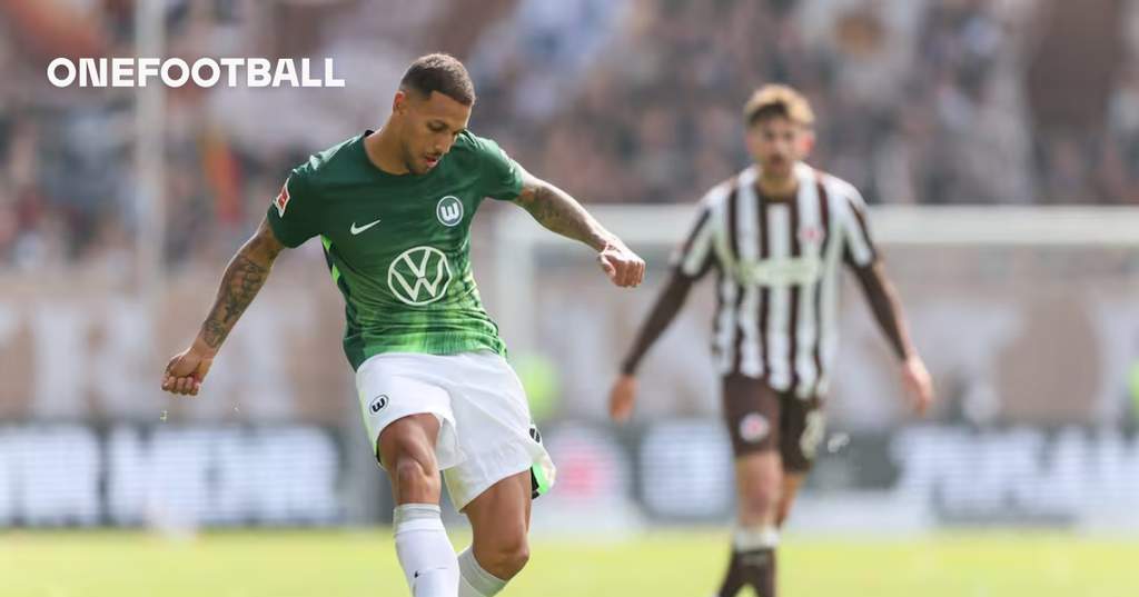 Pemain tengah VfL Wolfsburg Vinicius Souza saat berada di lapangan latihan mengenakan perlengkapan klub dengan latar belakang stadion utama.
